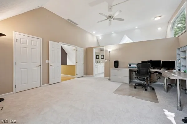 Office space featuring vaulted ceiling, light colored carpet, and ceiling fan