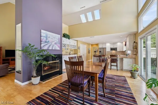 Dining area with a towering ceiling, light wood-style floors, and a high end fireplace