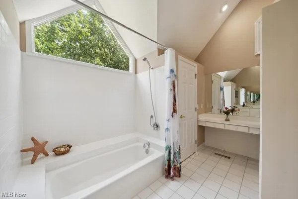 Full bathroom with vaulted ceiling, tile patterned flooring, vanity, and shower / bath combo with shower curtain