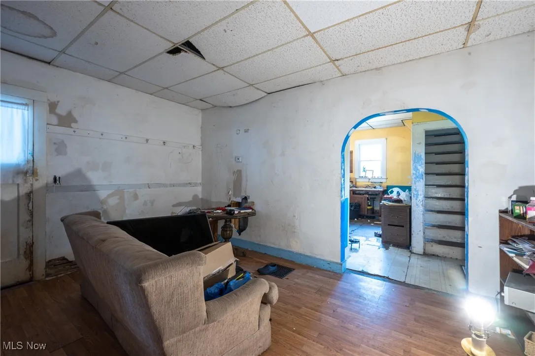 Living area with a paneled ceiling, wood finished floors, and arched walkways