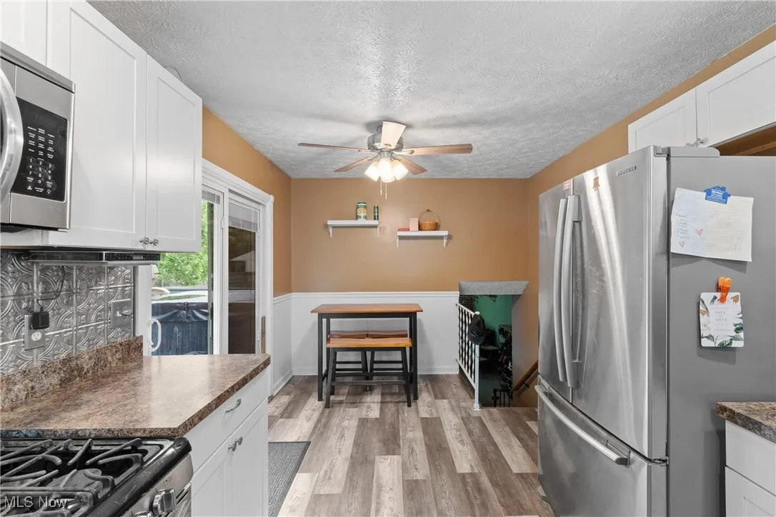 Kitchen featuring appliances with stainless steel finishes, a textured ceiling, ceiling fan, light wood-style flooring, and white cabinets