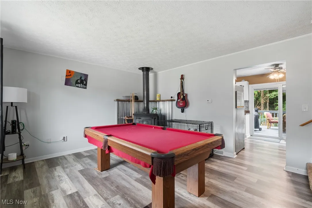 Playroom with a textured ceiling, wood finished floors, a wood stove, a ceiling fan, and billiards table