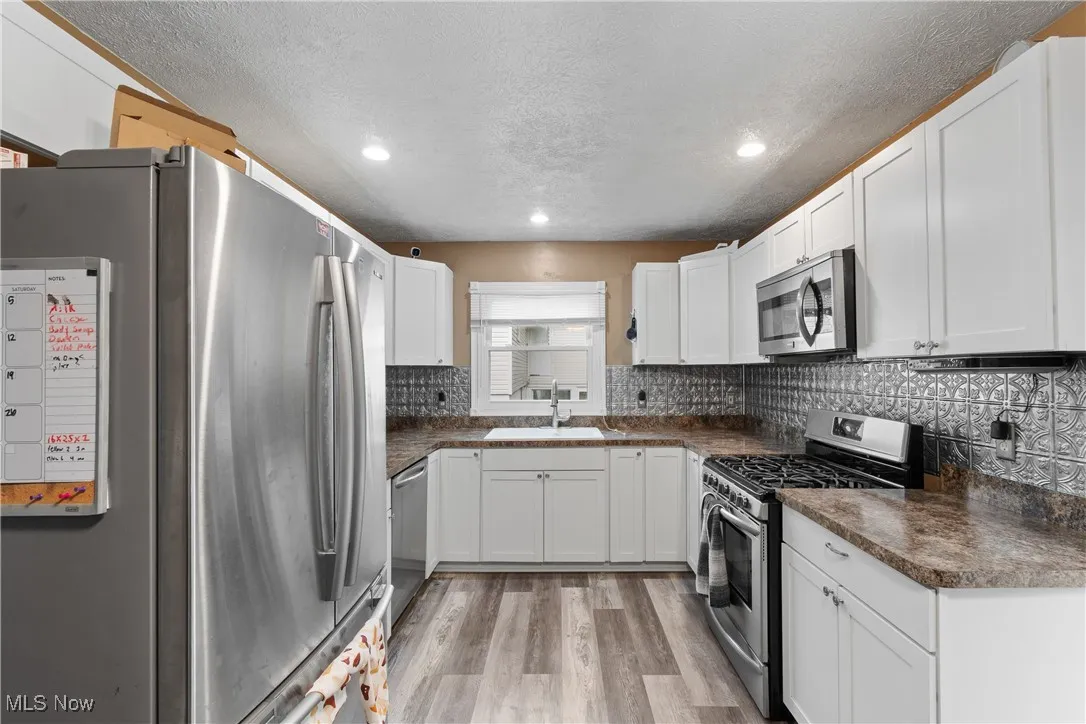 Kitchen with stainless steel appliances, dark countertops, light wood finished floors, white cabinets, and a textured ceiling