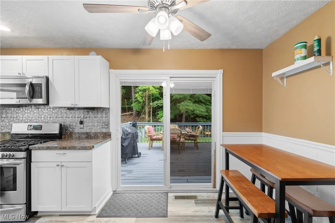 Kitchen featuring appliances with stainless steel finishes, a textured ceiling, a ceiling fan, dark countertops, and white cabinetry