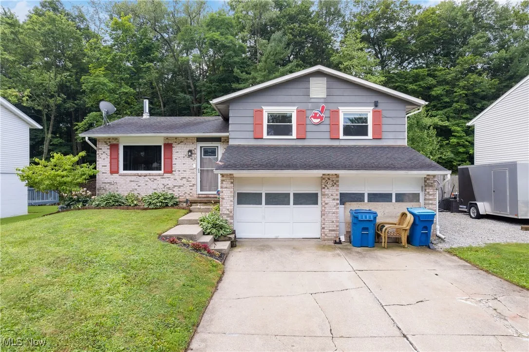 Split level home featuring concrete driveway, an attached garage, a front lawn, roof with shingles, and brick siding
