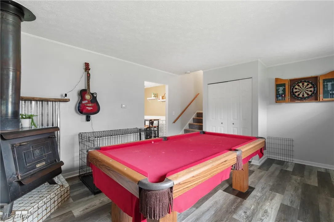 Recreation room with a wood stove, wood finished floors, a textured ceiling, and pool table