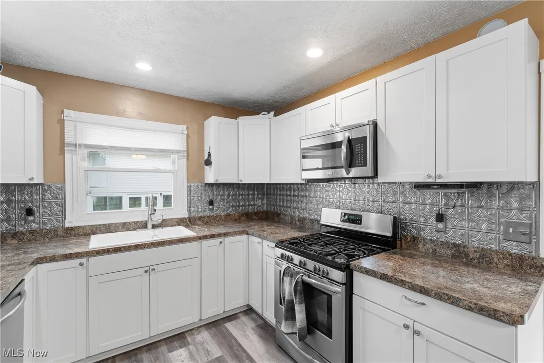 Kitchen featuring appliances with stainless steel finishes, white cabinets, a textured ceiling, backsplash, and light wood-type flooring
