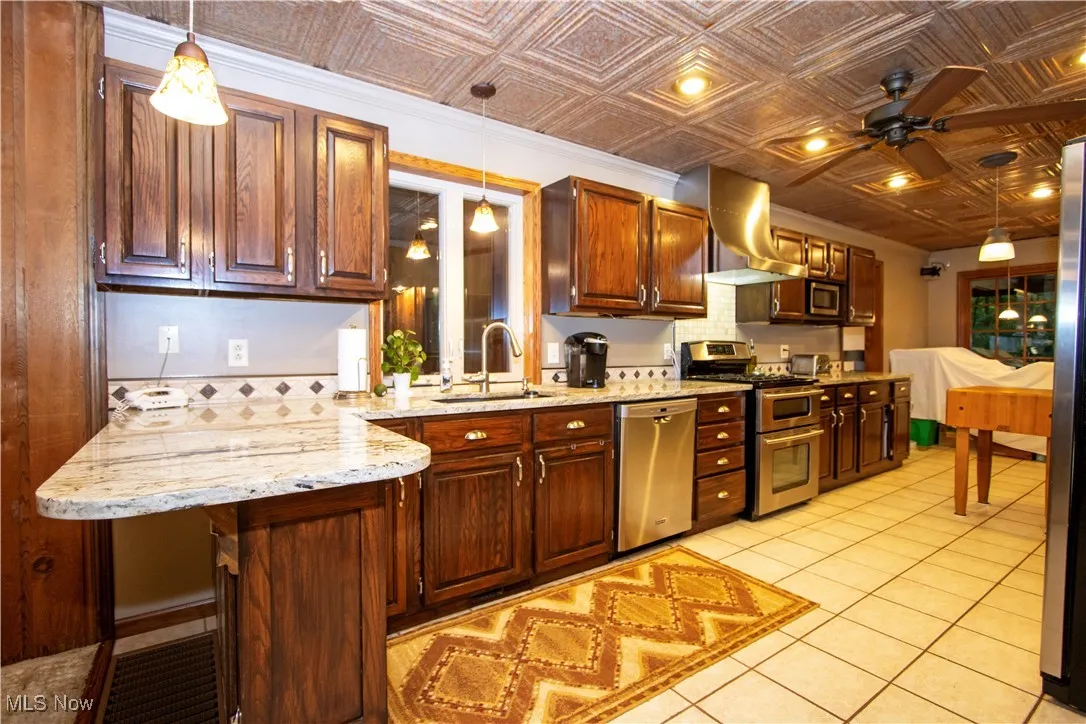 Kitchen featuring an ornate ceiling, stainless steel appliances, a ceiling fan, ventilation hood, and light tile patterned flooring