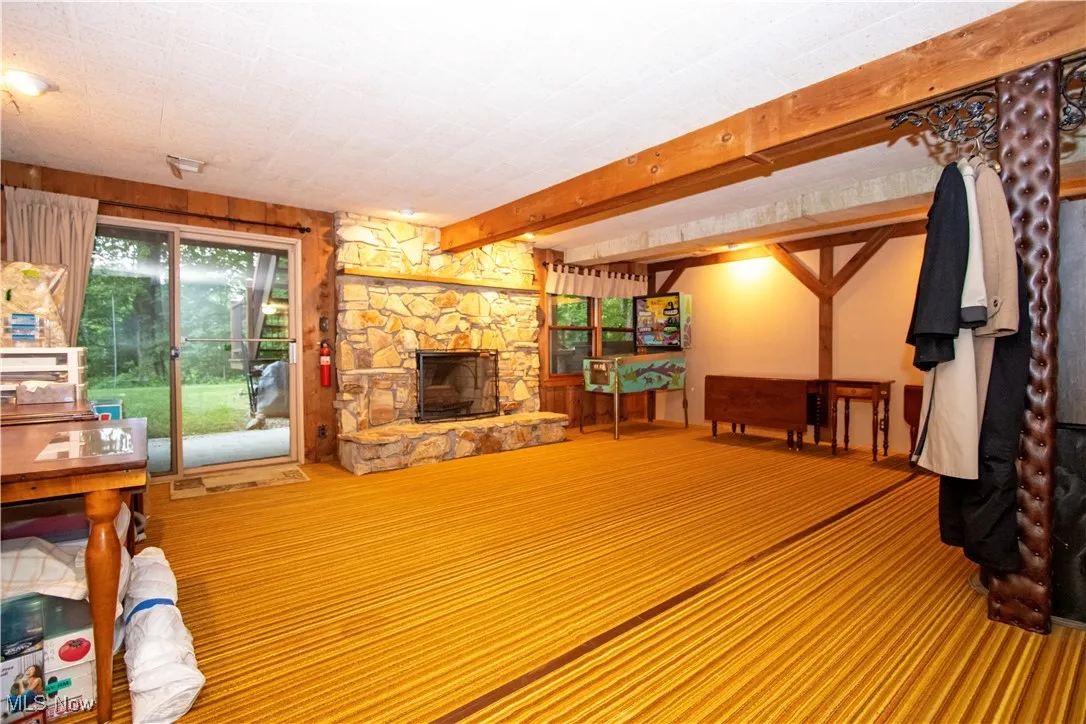 Living area with a stone fireplace, beamed ceiling, and carpet