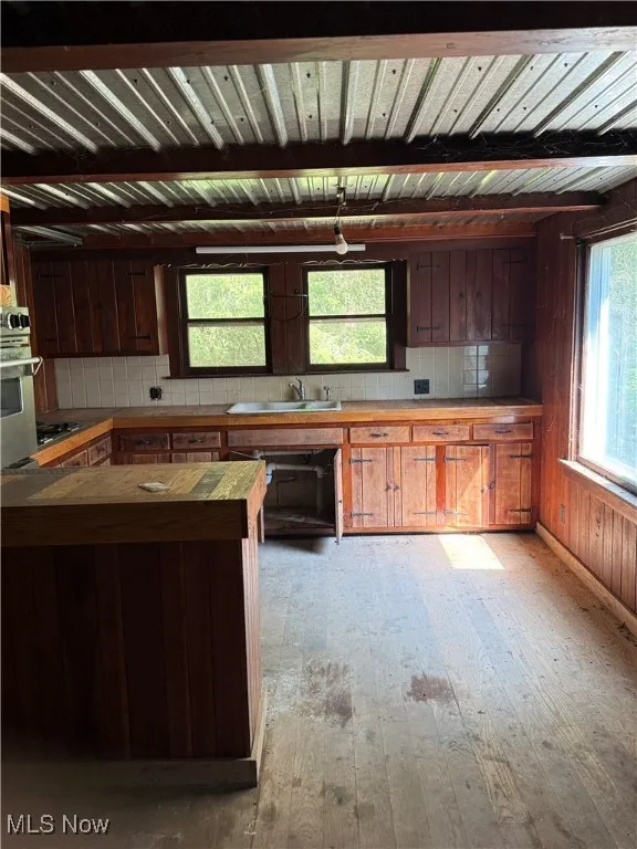 Kitchen featuring butcher block countertops, light wood-style flooring, a wood ceiling with exposed beams, wooden walls, and oven