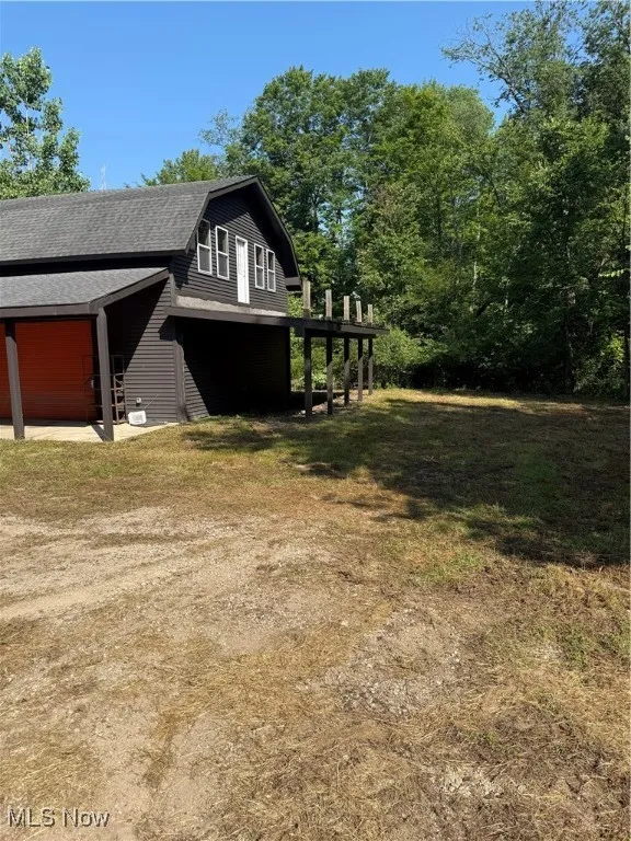 View of property exterior featuring a gambrel roof, a shingled roof, a garage, and a barn