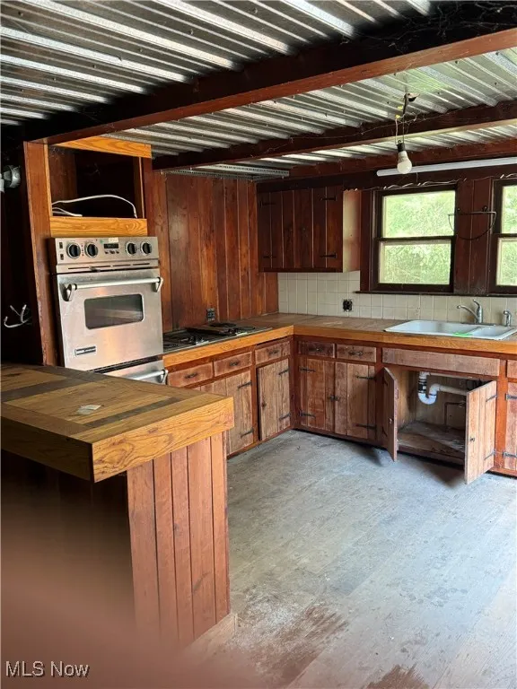 Kitchen featuring butcher block counters, light wood-style floors, stainless steel double oven, brown cabinets, and wood walls