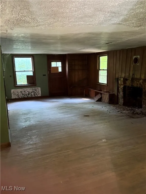 Unfurnished living room featuring a textured ceiling, a fireplace, and wooden walls