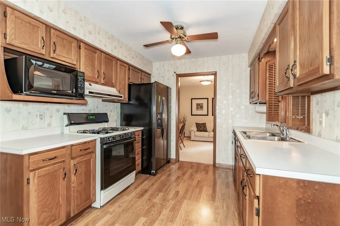 Kitchen with wallpapered walls, gas stove, black microwave, light wood finished floors, and ceiling fan