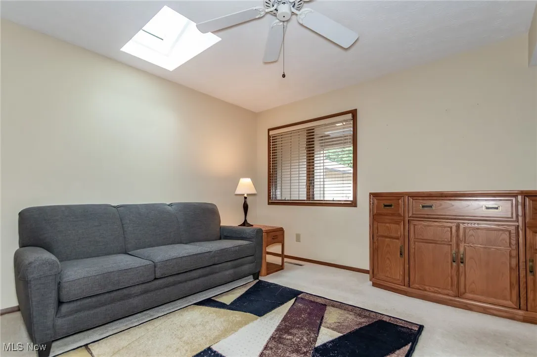 Living area with a skylight, light carpet, and a ceiling fan