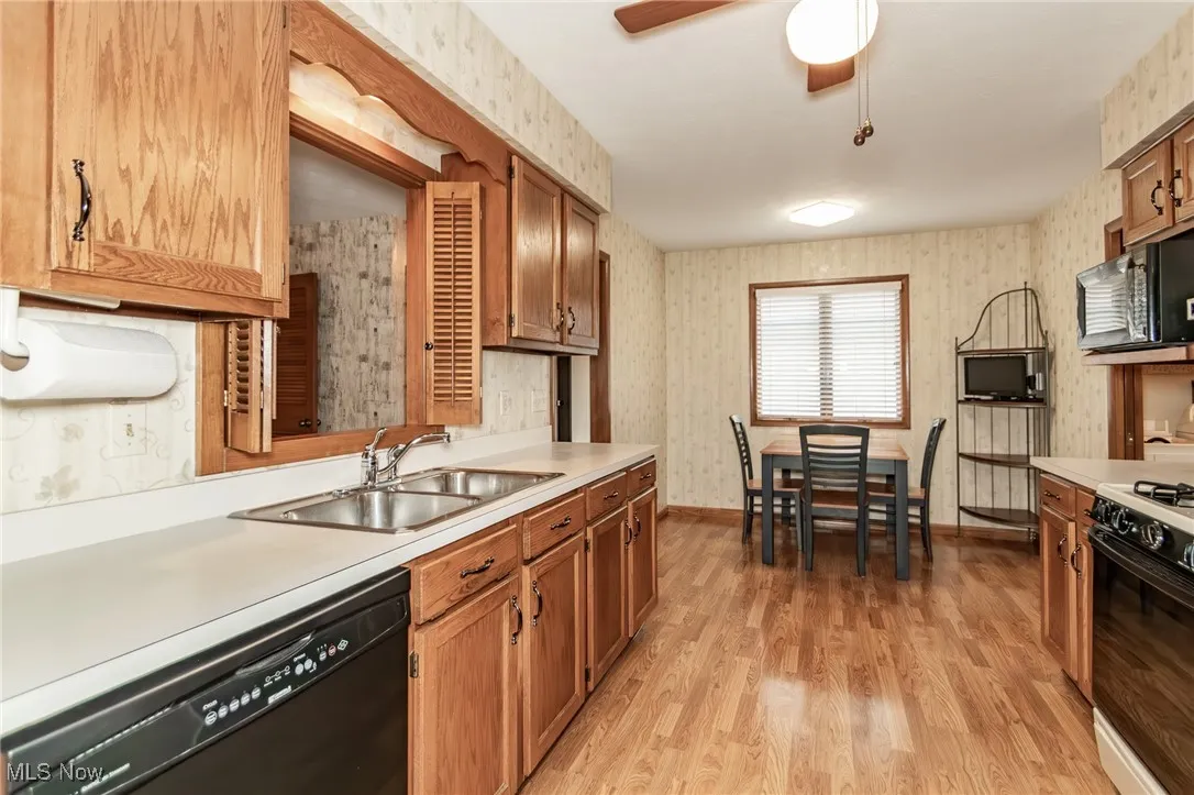 Kitchen with wallpapered walls, black appliances, light countertops, light wood finished floors, and ceiling fan