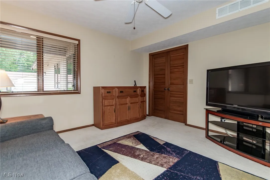 Carpeted living area with a ceiling fan and baseboards