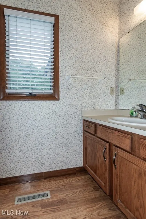 Bathroom featuring vanity, wood finished floors, and wallpapered walls
