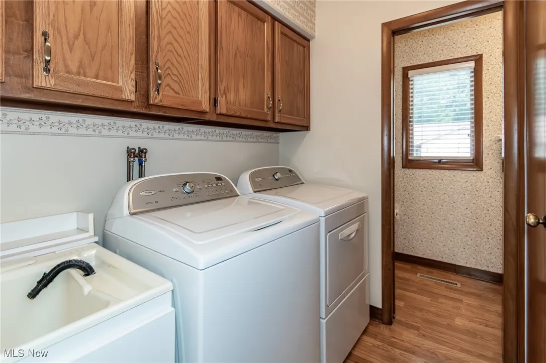 Laundry area featuring independent washer and dryer, cabinet space, light wood finished floors, and wallpapered walls