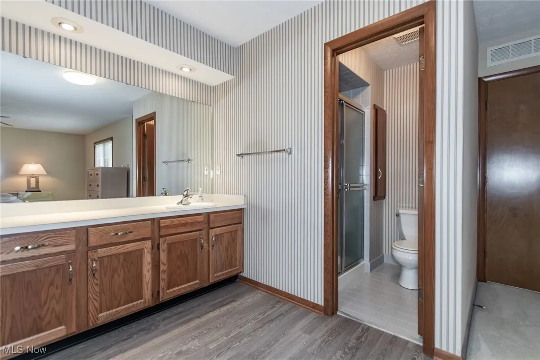 Bathroom featuring vanity, a stall shower, wood finished floors, and wallpapered walls