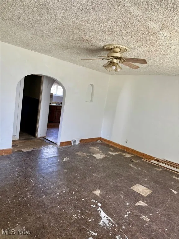 Spare room with arched walkways, a ceiling fan, and a textured ceiling