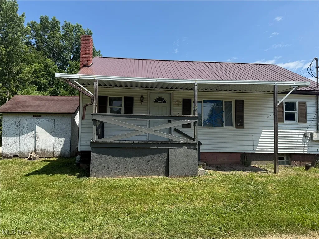 View of front facade featuring a chimney, a front lawn, and a metal roof