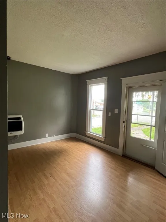 Empty room with wood finished floors, a textured ceiling, plenty of natural light, and heating unit
