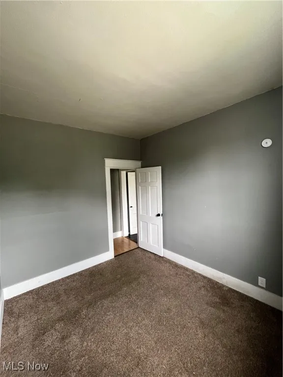 Unfurnished room with dark carpet and baseboards