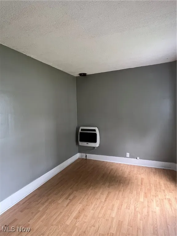 Unfurnished room featuring light wood-style floors, a textured ceiling, and heating unit