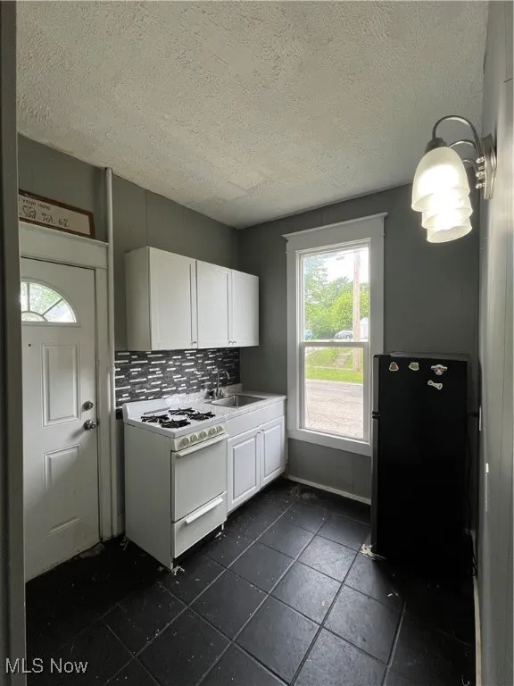 Kitchen featuring stove, white cabinetry, backsplash, a textured ceiling, and light countertops