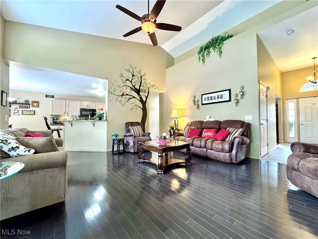Living area with high vaulted ceiling, ceiling fan, dark wood-type flooring, and a gas fireplace