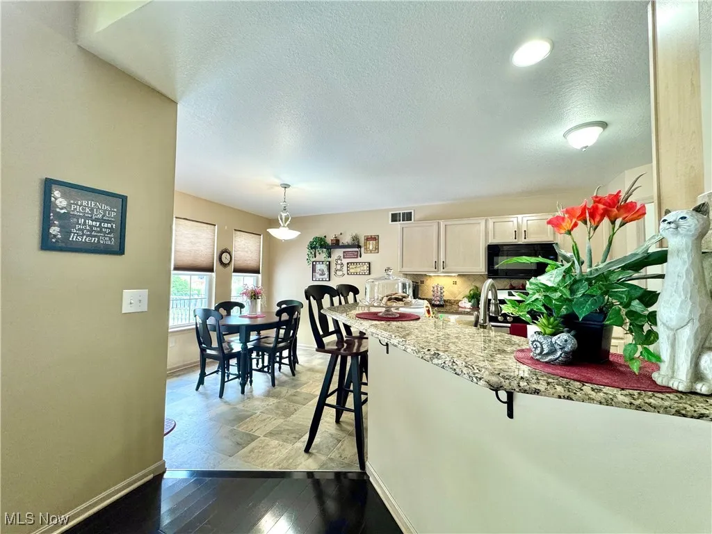 Kitchen with a breakfast bar area, light cabinets, all appliances, a textured ceiling, granite countertops and tasteful backsplash