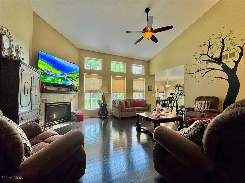Living area with high vaulted ceiling, a ceiling fan, dark wood-style flooring, and a gas fireplace
