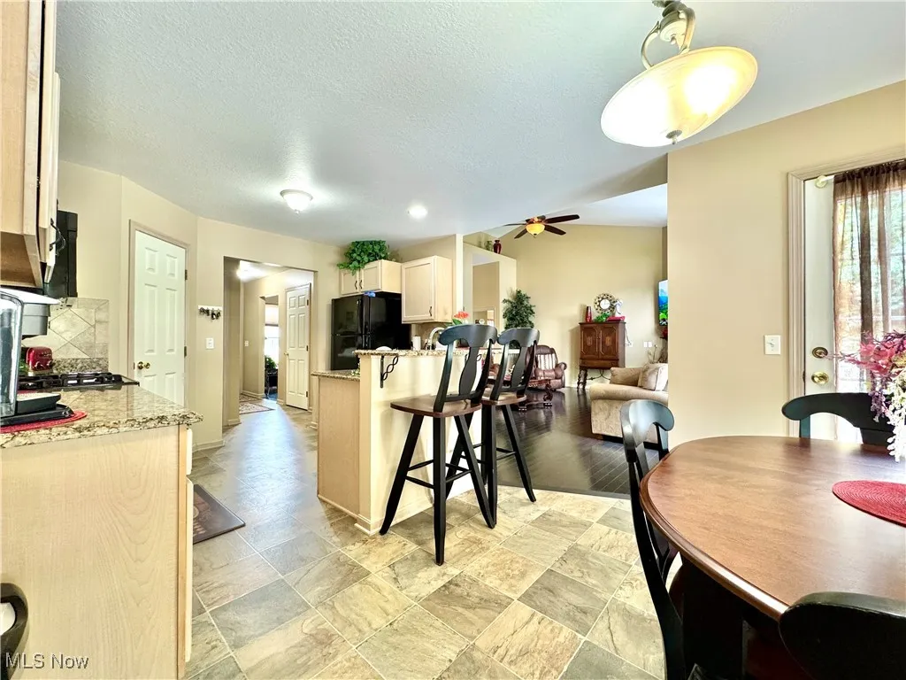 Kitchen featuring a breakfast bar, granite countertops, decorative backsplash, ceiling fan and light cabinets