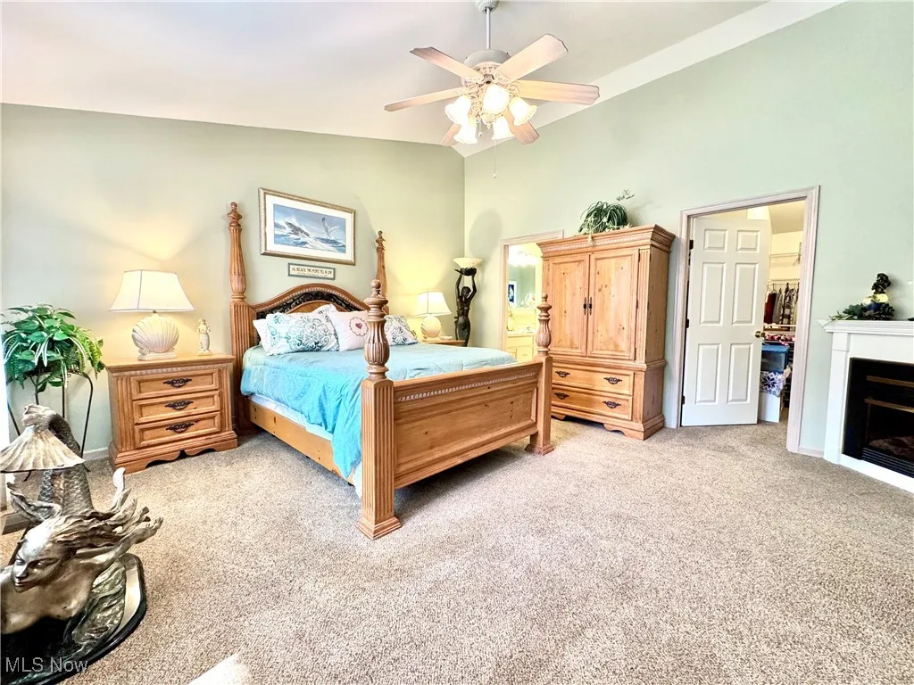 Bedroom featuring vaulted ceiling, light carpet, a fireplace, and ceiling fan