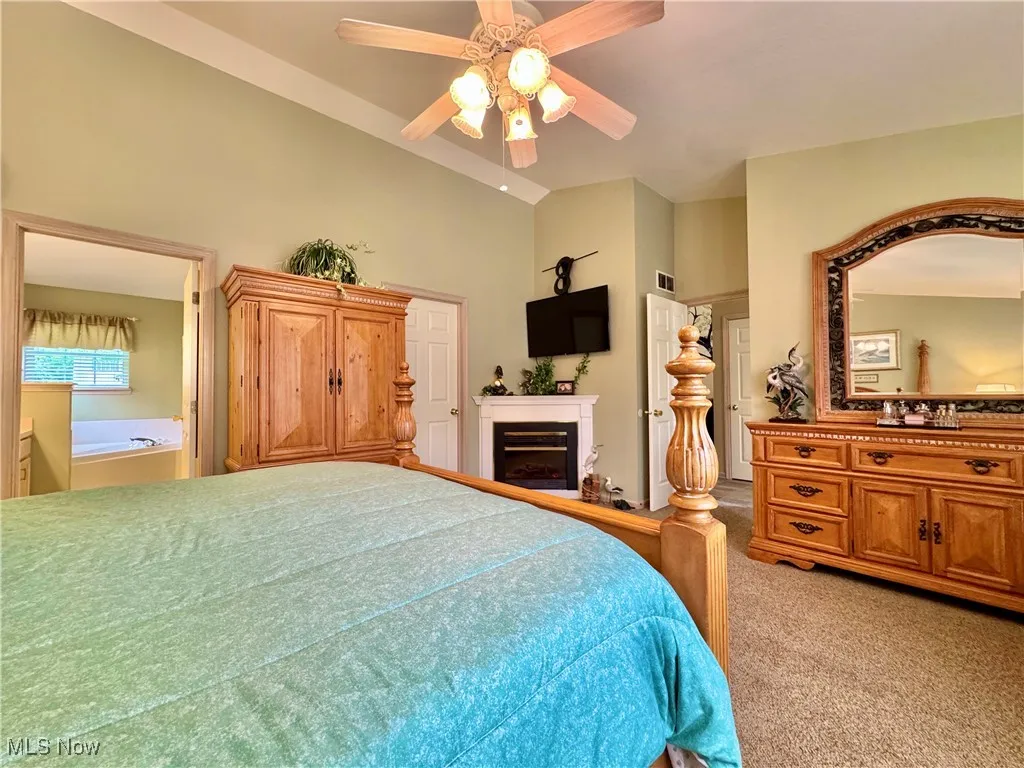 Bedroom with vaulted ceiling, light carpet, a fireplace, and ceiling fan