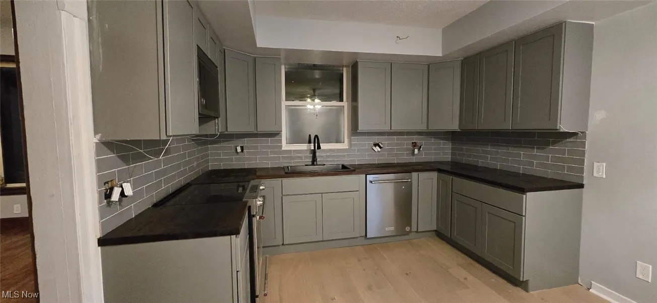 Kitchen with dark countertops, stove, light wood-type flooring, stainless steel dishwasher, and tasteful backsplash