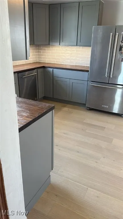 Kitchen featuring butcher block countertops, stainless steel appliances, light wood finished floors, and decorative backsplash