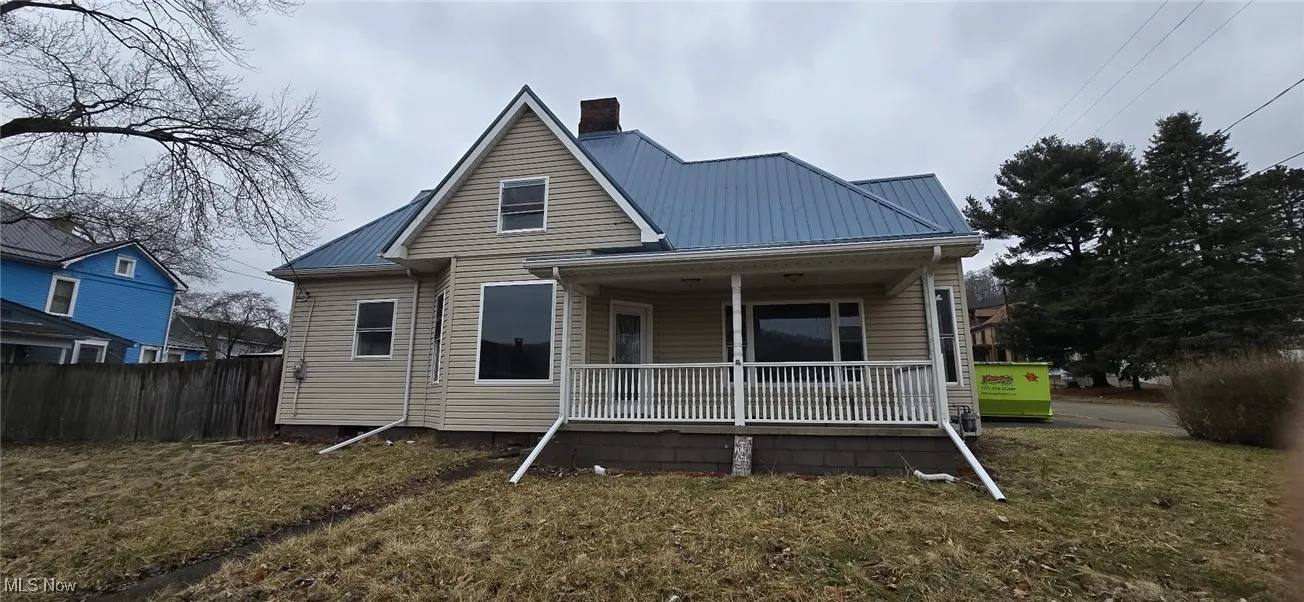 Rear view of property with covered porch, a chimney, and a metal roof