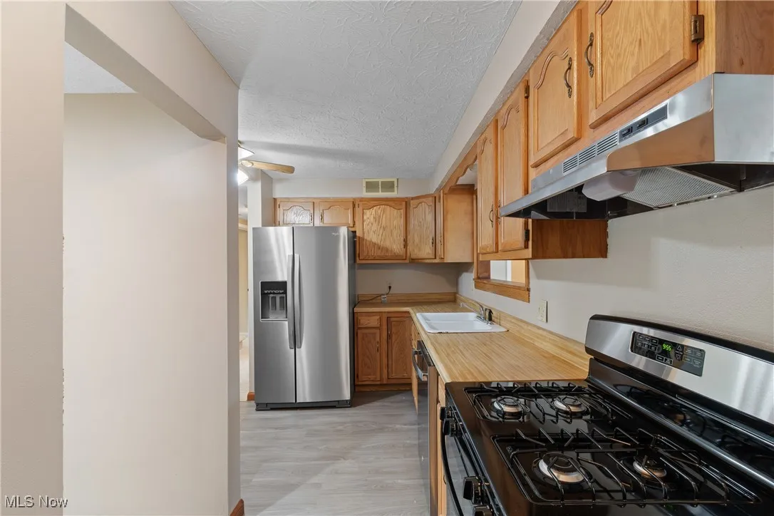 Kitchen with stainless steel appliances, light countertops, under cabinet range hood, a textured ceiling, and light wood-style flooring