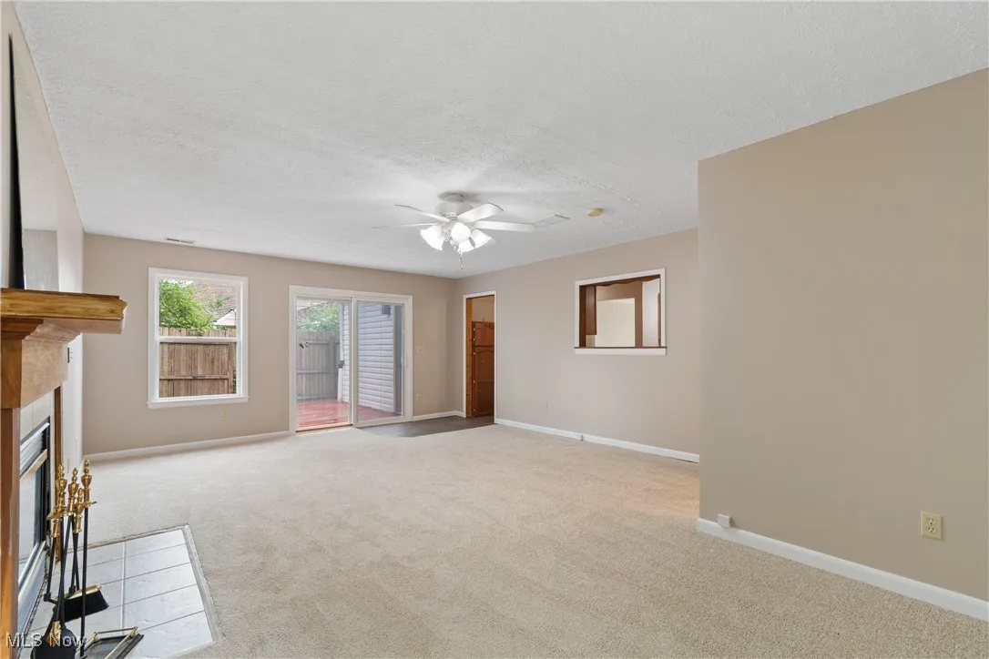 Unfurnished living room with carpet floors, a ceiling fan, a glass covered fireplace, and a textured ceiling