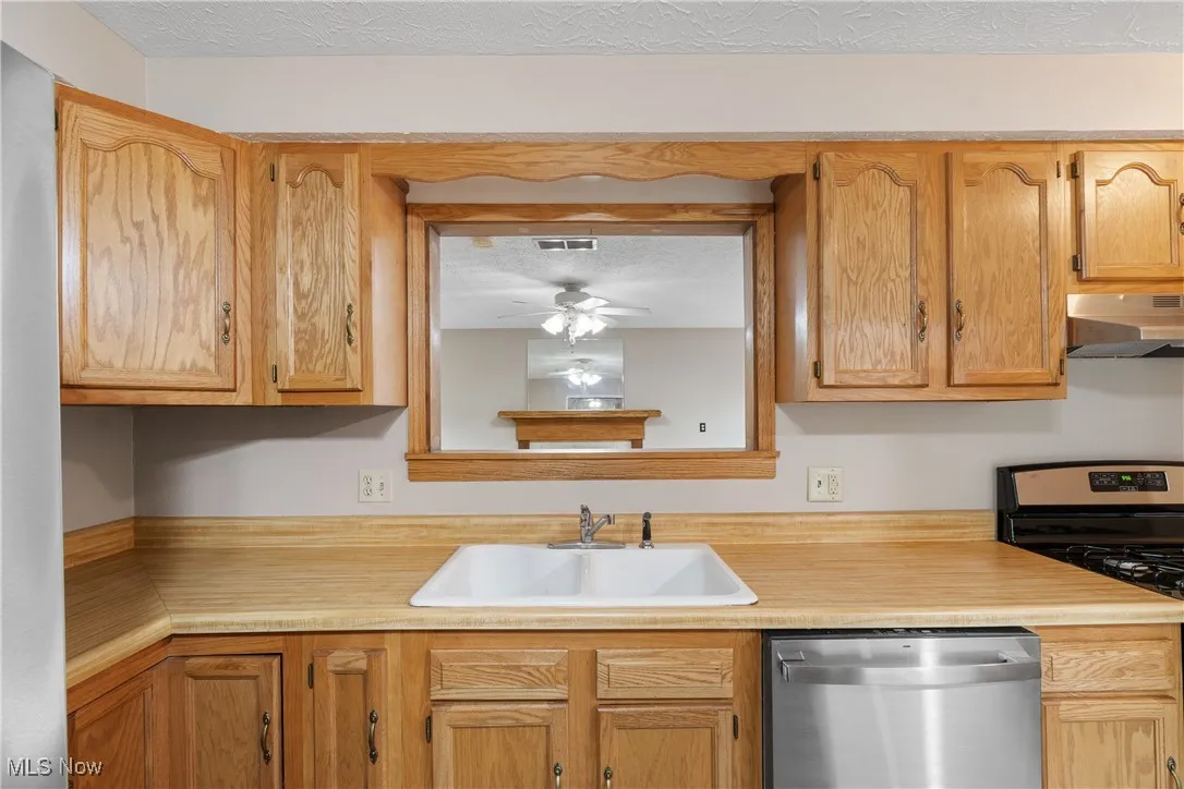 Kitchen featuring appliances with stainless steel finishes, light countertops, under cabinet range hood, ceiling fan, and a textured ceiling