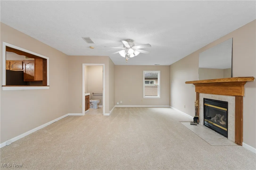 Unfurnished living room featuring light colored carpet, ceiling fan, a tiled fireplace, and a textured ceiling