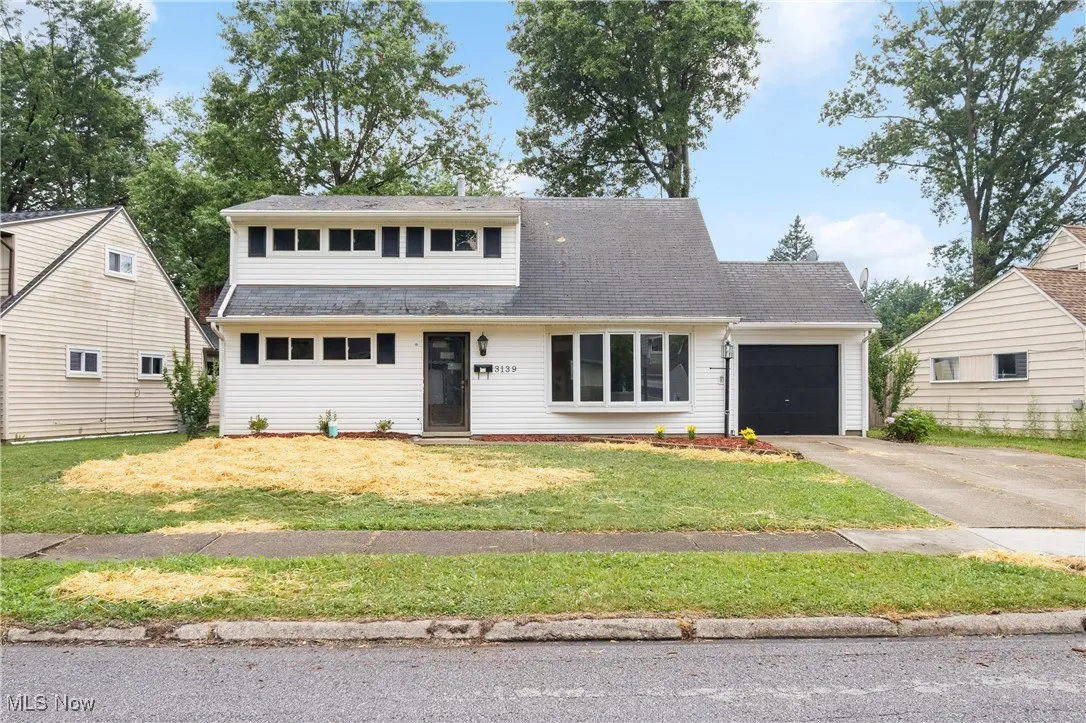 View of front of home with a garage, driveway, a front yard, and a shingled roof