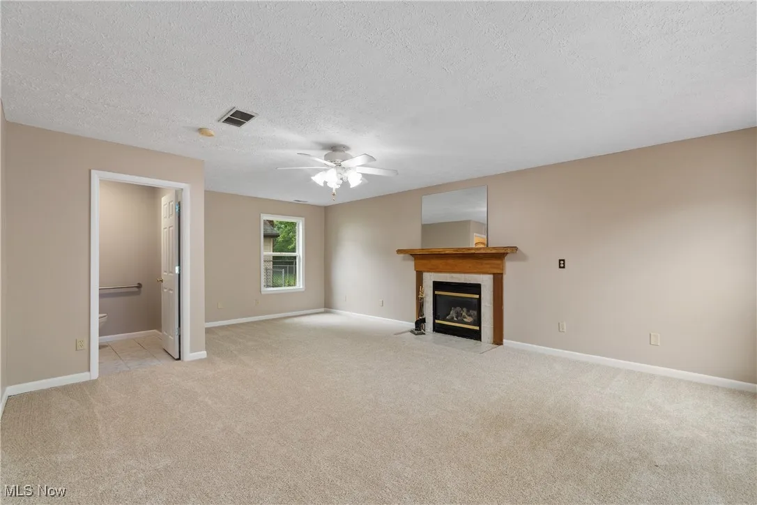 Unfurnished living room with light carpet, a textured ceiling, a fireplace, and ceiling fan