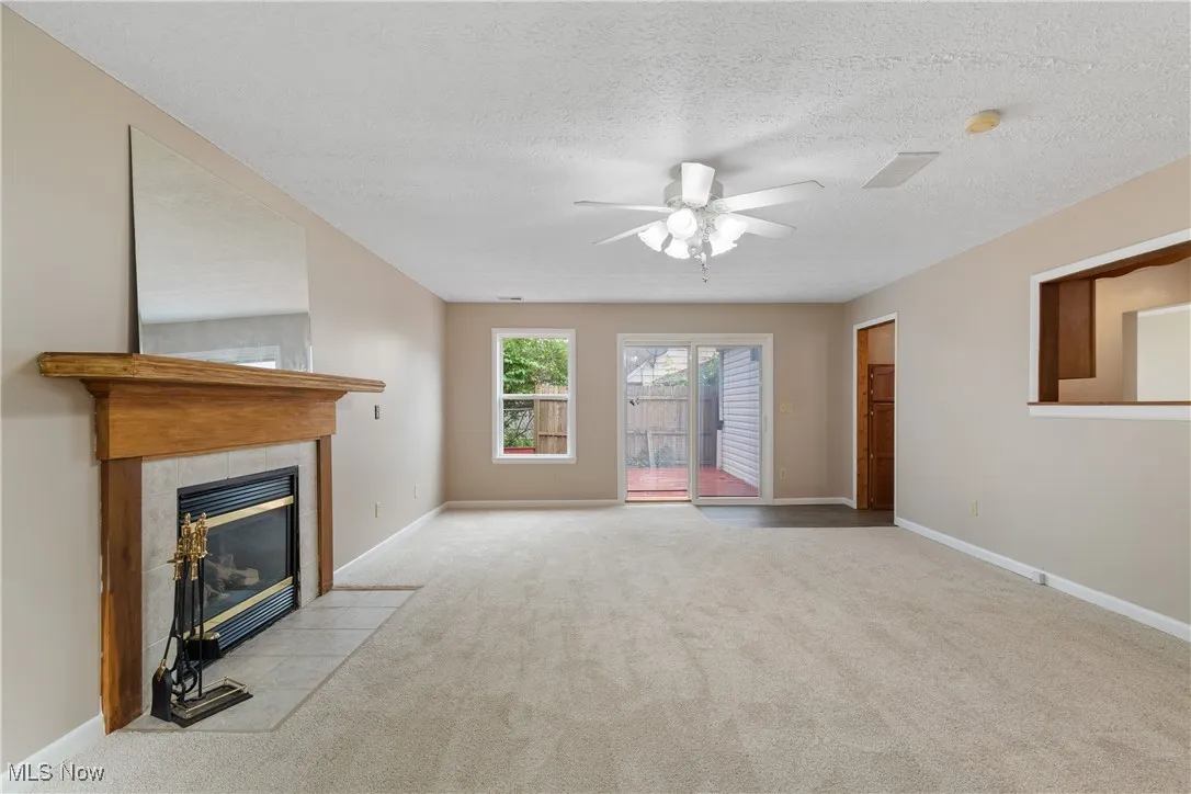 Unfurnished living room with carpet, a ceiling fan, a fireplace, and a textured ceiling