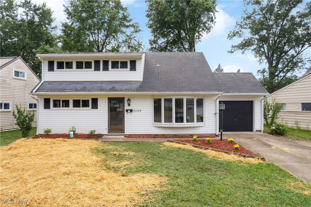 View of front of house with an attached garage, driveway, a front lawn, and a shingled roof