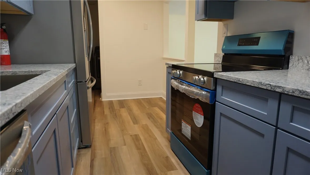 Kitchen featuring stainless steel appliances, light wood-style floors, and light stone countertops