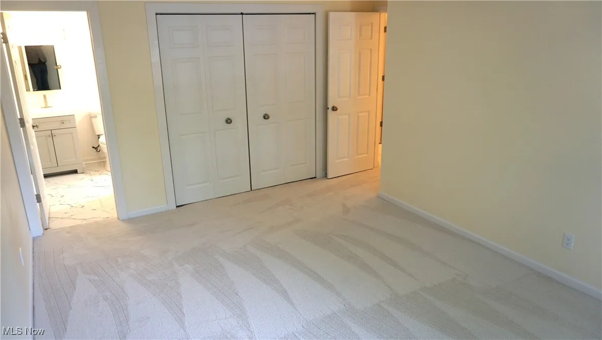 Unfurnished bedroom with light colored carpet, a closet, and connected bathroom