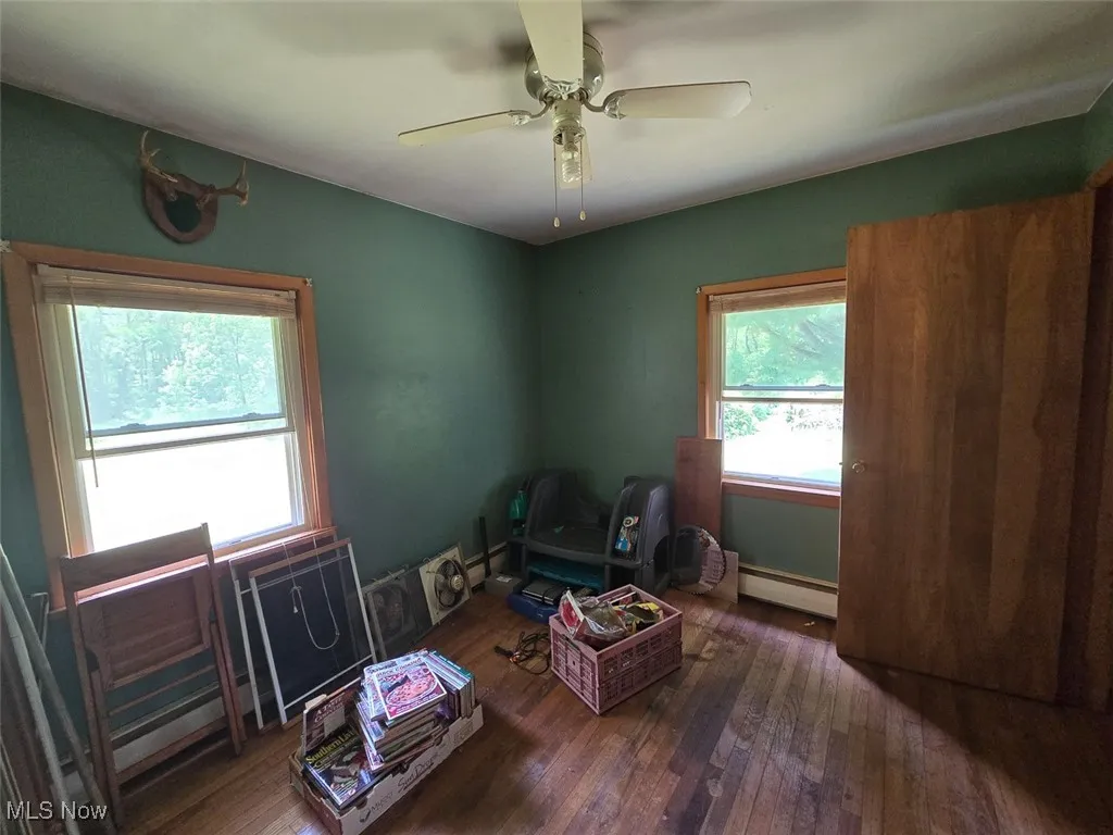 Bedroom featuring hardwood / wood-style floors, a baseboard heating unit, and a ceiling fan